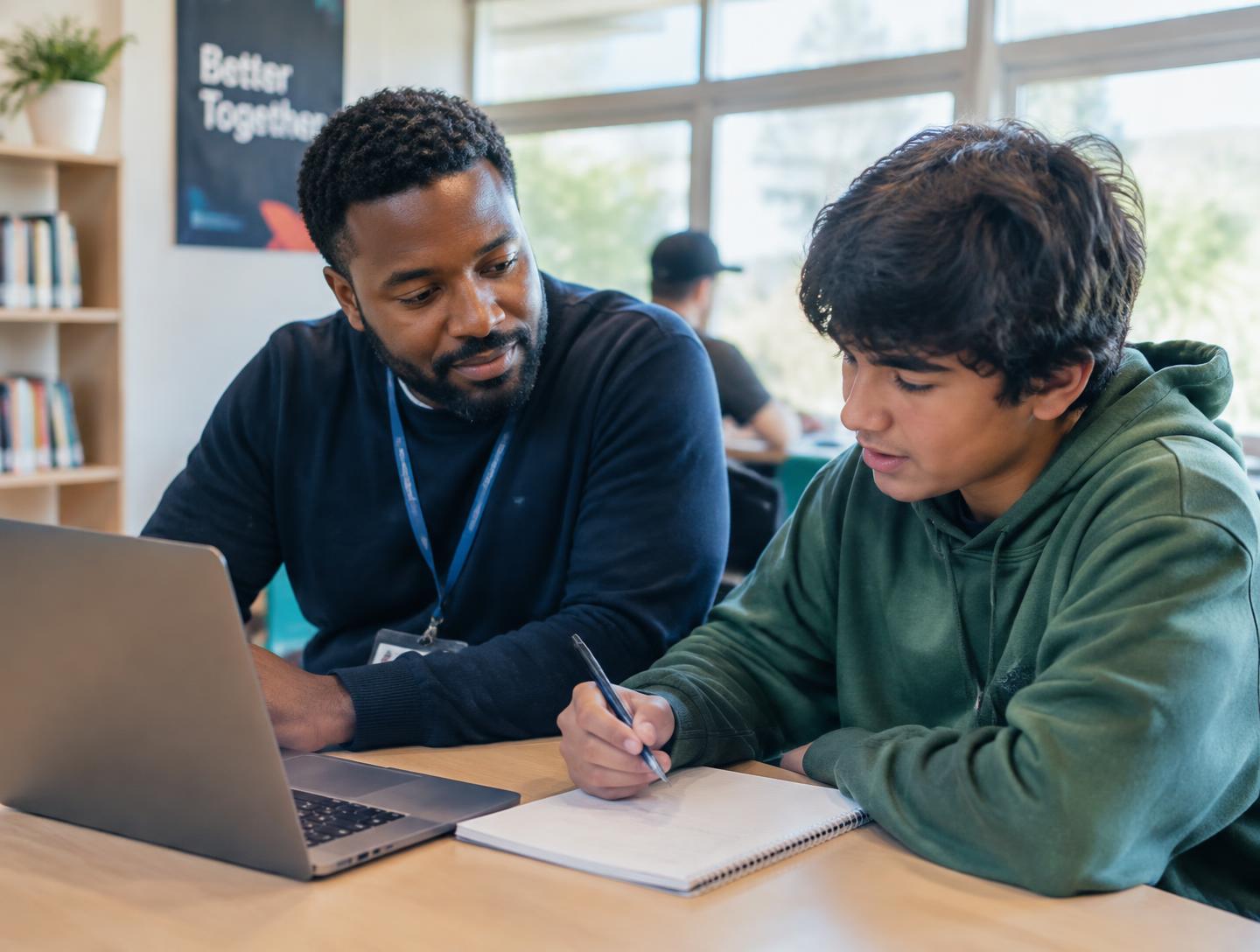 A mentor sitting beside a young person working through an idea together
